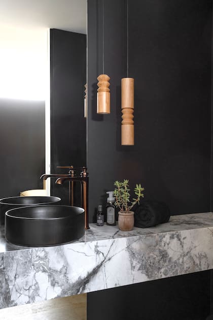 Toilette con pared pintada de negro y mesada de mármol ‘Invisible Grey’ (Canteras del Mundo) trabajada por Marmolería Forte. Bacha (Ferrum). Grifería de bronce (Drop Griferías). Lámparas colgantes ‘Ornette’ (Yucca).