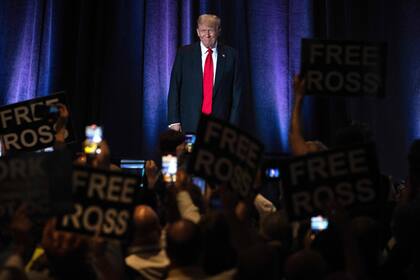 TOPSHOT - La gente sostiene carteles en los que se lee "Liberad a Ross" mientras el expresidente de Estados Unidos y candidato presidencial republicano Donald Trump llega para dirigirse a la Convención Nacional Libertaria en Washington