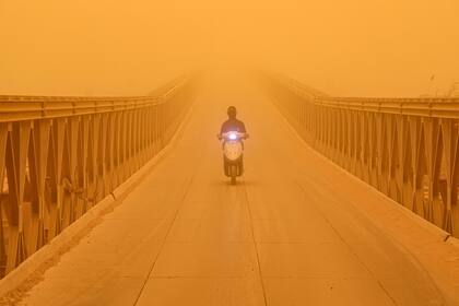 Un hombre conduce una moto a través de un puente en medio de una tormenta de arena que impide la visibilidad en Irak