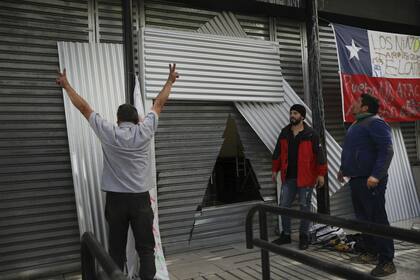 Trabajadores arreglan una cortina de hierro que protege a un banco, después de que se cortó un agujero triangular en la cortina en un intento de saqueo durante las protestas