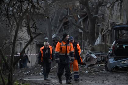 Trabajadores comunales caminan junto a casas residenciales que fueron parcialmente destruidas por una huelga rusa en la capital ucraniana