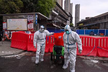 Trabajadores con trajes de protección caminan al lado del Mercado Mayorista de Mariscos de Huanan en Wuhan, China el 30 de marzo de 2020