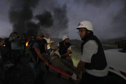 Trabajadores de defensa civil y un oficial de seguridad libanés transportan a un periodista que resultó herido por bombardeos israelíes, en la aldea fronteriza de Alma al-Shaab con Israel, en el sur del Líbano