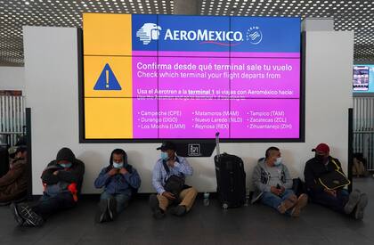 Trabajadores mexicanos, pasajeros de un vuelo cancelado hacia Canadá, esperan bajo un cartel de Aeroméxico en el aeropuerto Benito Juárez