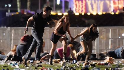 Tres asistentes al festival de música country en Las Vegas intentan refugiarse de la lluvia de balas disparadas por un tirador desde el hotel Mandalay Bay