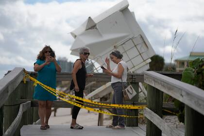 Tres mujeres visitan una playa para comprobar el alcance de los daños causados por el paso del huracán Nicole, incluyendo en un caseta de socorristas que fue desplazada hasta una duna, el 10 de noviembre de 2022, en Vero Beach, Florida. (AP Foto/Rebecca Blackwell)