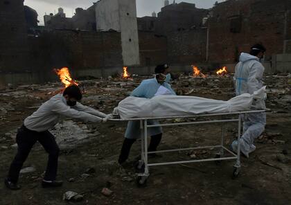 Tres operarios trasladan el cuerpo de un fallecido por COVID-19 para su incineración en un terreno convertido en crematorio, en Nueva Delhi