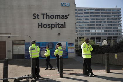 Tres policías a la izquierda y un guardia de seguridad a la derecha custodian una entrada frente al Hospital St Thomas en Londres, donde el primer ministro británico Boris Johnson está hospitalizado