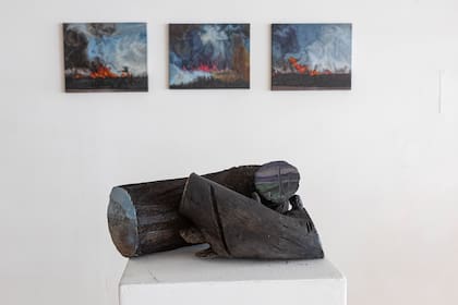 Troncos quemados e intervenidos con escenas; detrás, imágenes inspiradas en los incendios en las islas rosarinas en 2022