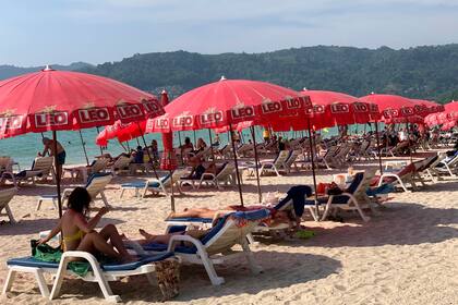Turistas disfrutan baj sombrillas en la Playa Patong en Phuket, Tailandia, el 11 de marzo del 2022. Miles de turistas rusos están varados en los balnearios de Tailandia debido a la guerra en Ucrania, muchos de ellos incapaces de agar sus cuentas o regresar al país debido a sanciones y vuelos cancelados. (AP Foto/Salinee Prab)