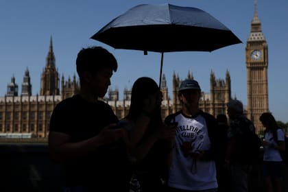 Turistas se resguardan del sol bajo una sombrilla, con la torre comúnmente conocida como "Big Ben" de fondo, en el centro de Londres, el 26 de mayo de 2026, mientras la ola de calor se extendía por partes del sureste de Inglaterra y Londres (Adrian Dennis / AFP)