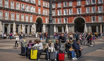 Turistas sentados en un banco público en la Plaza Mayor en el centro de Madrid, España