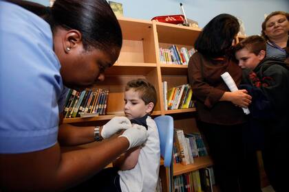Una enfermera le aplica una curita a Alexander Milan, de 5 años, después de recibir una vacuna contra la influenza H1N1 mientras su hermano espera su turno junto a su madre