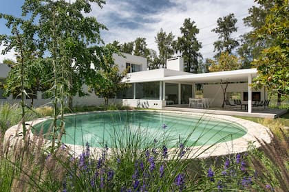 Ubicada en el centro del jardín, la pileta tiene un borde elevado revestido en piedra Mar del Plata blanca y está rodeada de canteros con plantas autóctonas.
