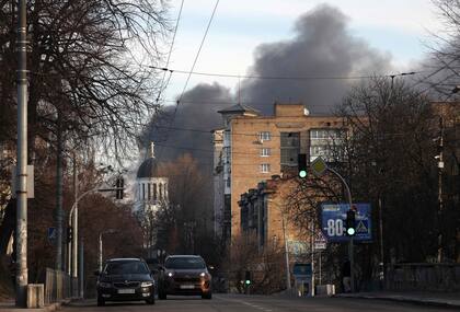 Los autos transitan por la calle mientras el humo se eleva de un incendio después de un ataque con cohetes en el centro de Kiev el 29 de diciembre de 2023, en medio de la invasión rusa a Ucrania.