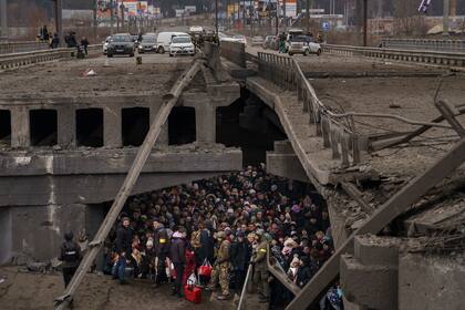 Ucranianos esperan debajo de un puente destruido mientras tratan de escapar cruzando el río Irpin, a las afueras de Kiev, Ucrania