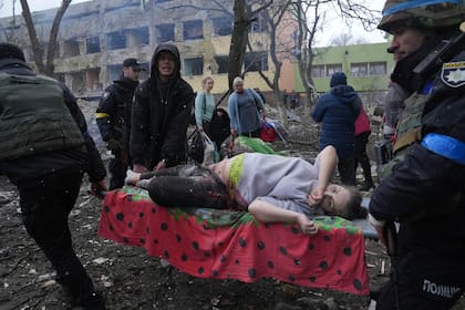Empleados y voluntarios de emergencia ucranianos llevan a una mujer embarazada herida desde el hospital de maternidad dañado por los bombardeos en Mariupol