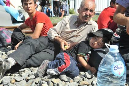 Un abuelo con su nieto descansan sobre las vías del tren que conduce a Hungría