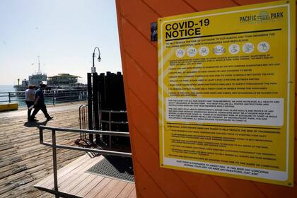 Un afiche con instrucciones de comportamiento por el Covid-19 en el Pacific Park en el muelle de Santa Mónica