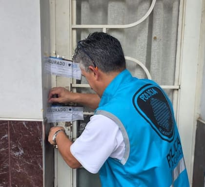 Un agente de la Policía de la Ciudad coloca las fajas de clausura en la puerta de la vivienda de Villa Crespo donde funcionaba el consultorio clandestino
