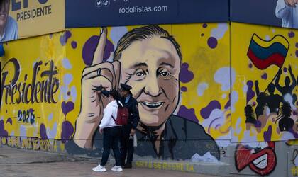 Un agente de seguridad privada da indicaciones a una mujer frente a un mural con la imagen del candidato independiente colombiano Rodolfo Hernández, conocido como "el Trump colombiano", en Bogotá, el 23 de mayo de 2022.