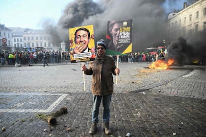 Un agricultor sostiene pancartas junto a tractores y una hoguera cerca del Parlamento Europeo, en la Plaza de Luxemburgo, durante una protesta campesina para denunciar las reformas de la Política Agrícola Común (PAC) y acuerdos comerciales como el Mercosur. Esta protesta se llevó a cabo en Bruselas el 18 de diciembre de 2025