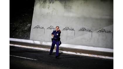 Un oficial de policía hace gestos hacia un artista brasileño, conocido como Iaco, después de haber escrito "doria" en referencia al alcalde de Sao Paulo, Joao Doria, en un muro de la Avenida 23 de Mayo en San Pablo, Brasil
