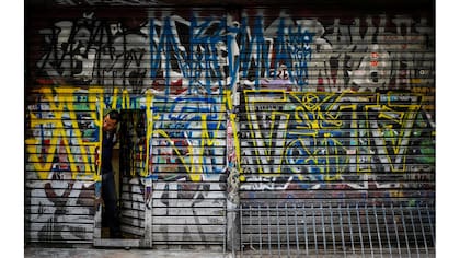 Un hombre mira para afuera de su local pintado por pichadores