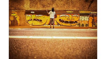 Un "pichador" posa frente a un mural de un artista brasileño "Humanos", en una calle de San Pablo. Las dos caras del mural se refieren a un "pichador" y un artista de grafiti