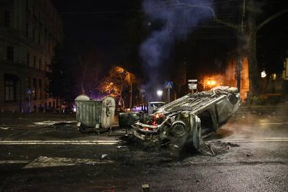 Un auto de policía arde cerca de los restos de la barricada tras los enfrentamientos entre manifestantes y policías en una calle cercana al edificio del Parlamento georgiano en Tiflis, Georgia, jueves 9 de marzo de 2023. 