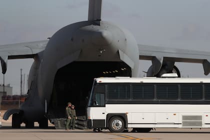 Un avión militar a la espera de que migrantes desciendan de un ómnibus para abordar en Fort Bliss, en Texas, antes de ser deportados a Guatemala