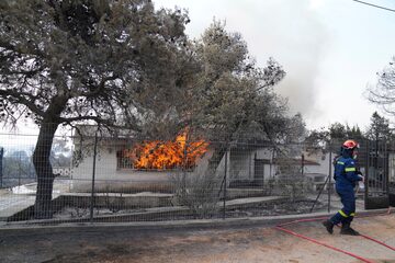 Un bombero camina fuera de una casa mientras se quema durante un incendio forestal en el área de Thea a unos 60 kilómetros al noroeste de Atenas, Grecia