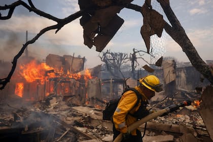 Un bombero combate un incendio alrededor de una estructura calcinada en el vecindario de Pacific Palisades, en Los Ángeles, California, el miércoles 8 de enero de 2025. (AP Foto/Etienne Laurent)