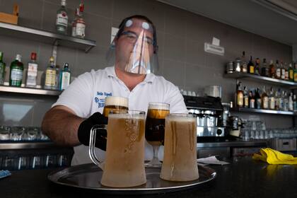 Un camarero con un protector facial prepara algunas cervezas para servir en la terraza del bar La Malvarrosa en Valencia, el 19 de mayo de 2020, ya que algunas provincias españolas pueden aliviar las restricciones de bloqueo en medio del coronavirus