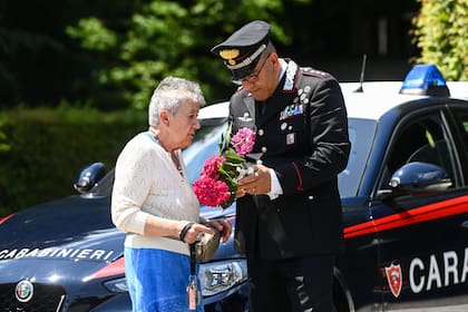 Un carabinero asiste a una mujer que se acercó a dejar una ofrenda de flores por Berlusconi
