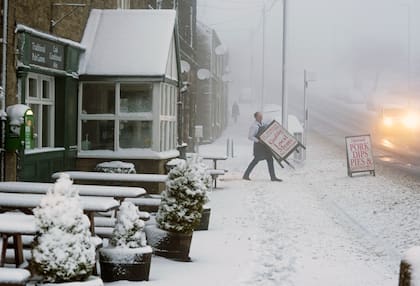 Un carnicero se lleva el letrero de su tienda a través del pavimento nevado en Tow Law, Condado de Durham, Gran Bretaña
