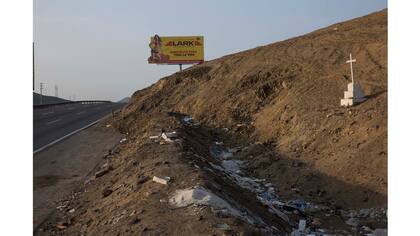 Un cartel publicitario de materiales de construcción se encuentra a lo largo de la Carretera Panamericana, donde una cruz marca el lugar donde alguien fue asesinado, en el lado sur de Lima