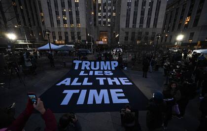 Un cartel que dice "Trump miente todo el tiempo" se despliega en la acera frente a la oficina del fiscal del distrito de Manhattan en la ciudad de Nueva York el 30 de marzo de 2023. 