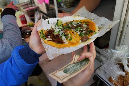 Un ciclista recibe comida de la vendedora ambulante Yulisa Robles, derecha, en Gage Park durante la Serie de Recorridos en Bicicleta con Vendedores Ambulantes en Chicago, el domingo 2 de noviembre de 2025. (AP Foto/Nam Y. Huh)