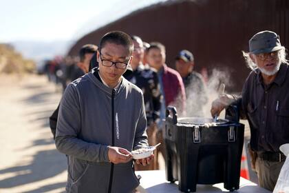 Un ciudadano chino recibe avena cocida de manos de un voluntario mientras aguarda junto con otras personas a solicitar asilo tras cruzar la frontera con México, el martes 24 de octubre de 2023, cerca de Jacumba, California