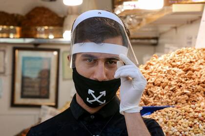 Un comerciante iraní, que usa equipo de protección personal en medio de la pandemia de coronavirus, espera a los clientes en el mercado del Gran Bazar en la capital, Teherán
