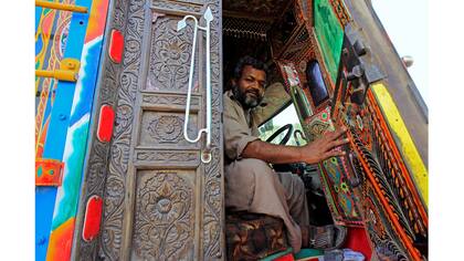 Un conductor mantiene abierta la puerta de la cabina de madera tallada de su camión decorado en Faisalabad