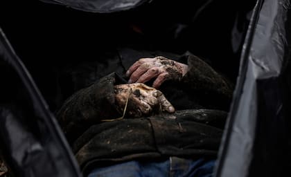 Un cuerpo se ve parcialmente mientras se recolectan bolsas para cadáveres en un cementerio de Bucha.