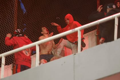 Un ejemplo entre muchos: un simpatizante sangrante y desnudado de Universidad de Chile es pateado por uno de Independiente; unos empezaron, otros respondieron y la barbarie se apoderó de una noche de fútbol.. (Photo by Alejandro PAGNI / AFP)