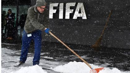 Un empleado de la FIFA trabaja quitando la nieve en la puerta de la sede del organismo