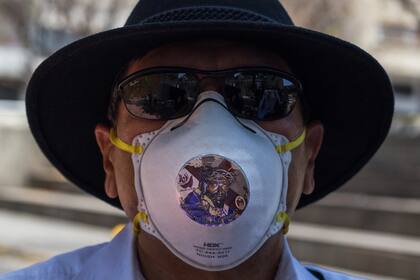 Un fiel católico usa una mascarilla N95 con una imagen de Nazareno de San Pablo afuera de la Catedral de Santa Teresa cerrada el domingo de Pascua después de que se cancelaron las celebraciones de la Semana Santa en medio de la propagación de la enfermedad Covid-19 en Caracas, Venezuela