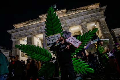 Un fumador de marihuana fuma un porro delante de una planta de marihuana gigante simulada durante una manifestación frente a la Puerta de Brandeburgo de Berlín para conmemorar la entrada en vigor en Alemania el 1 de abril de 2024 de una ley que permite a los adultos llevar hasta 25 gramos de cannabis seco y cultivar hasta tres plantas de marihuana en casa.