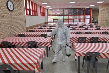 Un funcionario de salud que usa equipo de protección rocía desinfectante en una cafetería de una escuela secundaria en Seúl el 11 de mayo de 2020
