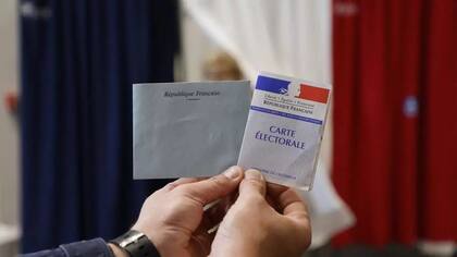 Un funcionario del colegio electoral sostiene una tarjeta electoral y una papeleta en un colegio electoral de Le Touquet, para la segunda vuelta de las elecciones regionales francesas del 27 de junio de 2021. AFP - LUDOVIC MARIN