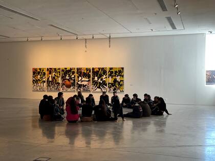 Un grupo de estudiantes escucha al educador con atención, junto a una obra de Washington Cucurto